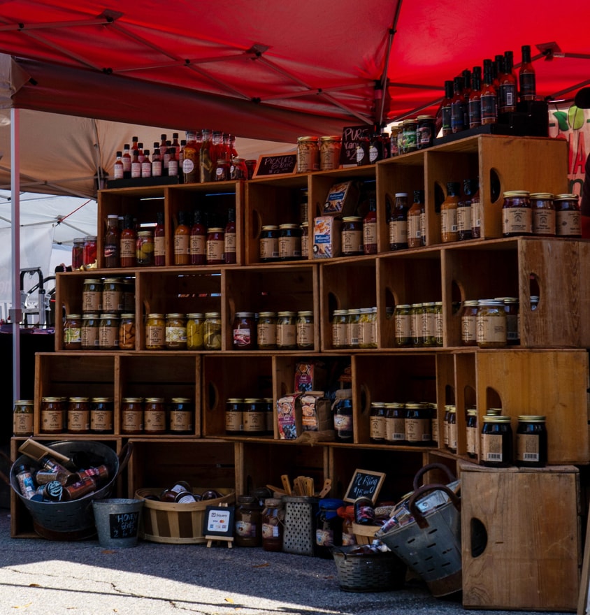 Market vendor display with jarred goods and sauces under a red tent