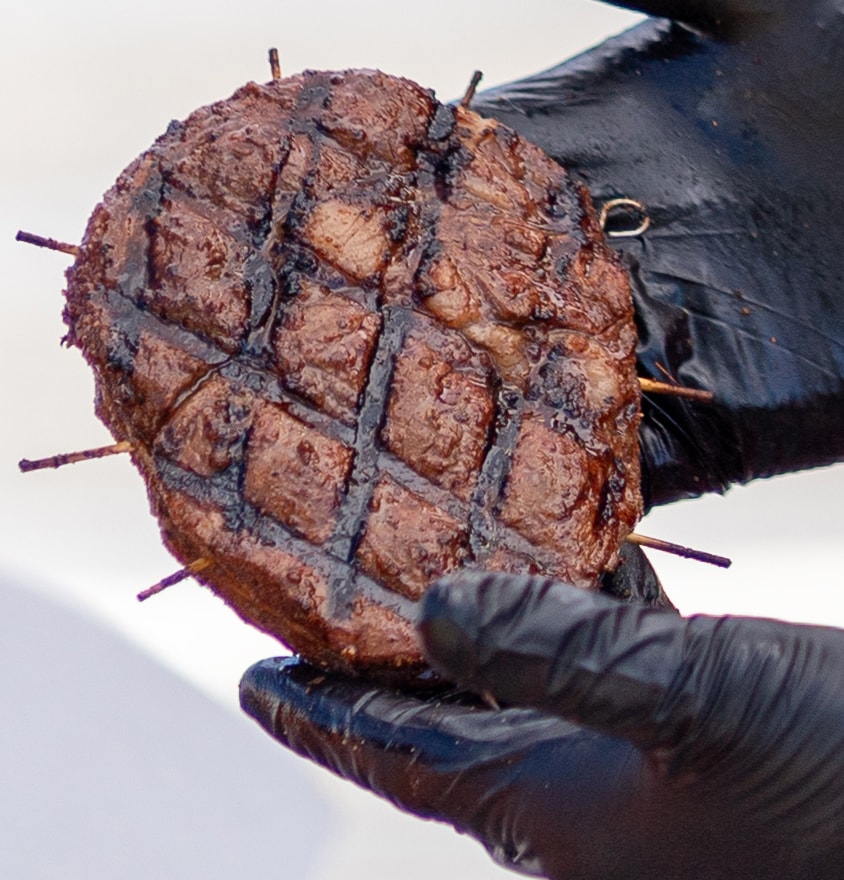 Perfectly grilled steak held up with black gloves at the cook-off